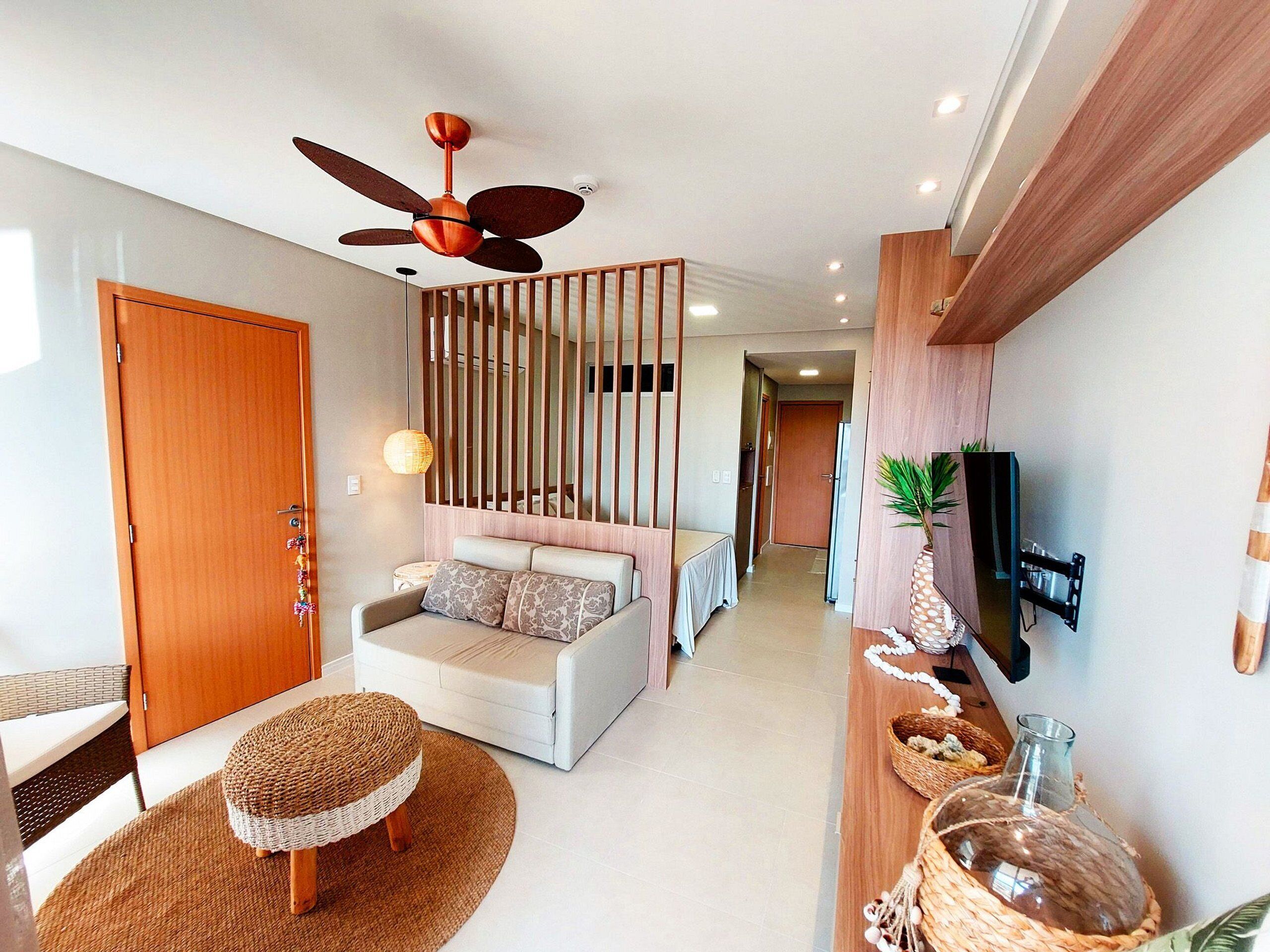 A modern living room with a sofa, a wooden partition, a ceiling fan, and a television mounted on the wall.