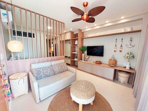 A modern living room with a sofa, ottoman, TV, and decorative items. - Eco Resort - Igrejinha de Carneiros (Tamandaré)