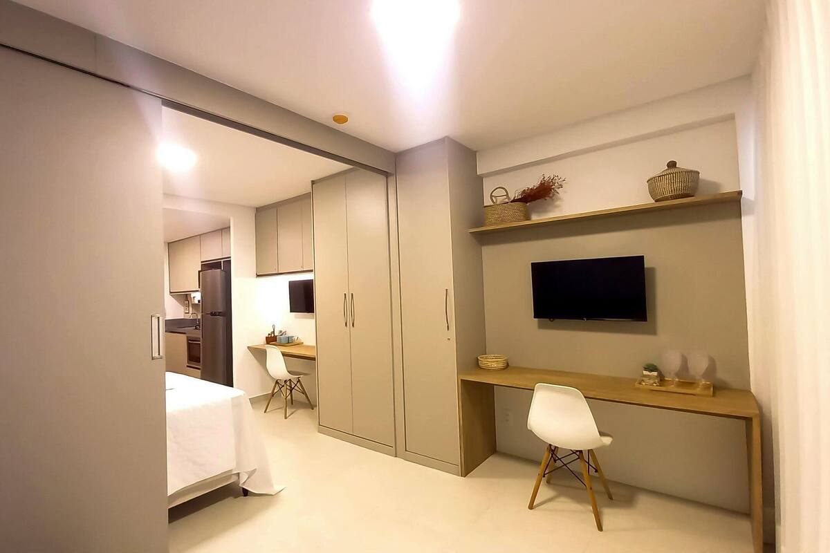 A modern bedroom with a bed, a desk, a chair, a TV, and a wardrobe.