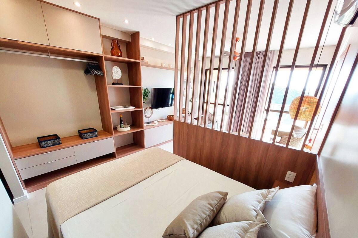 A bedroom with a bed, a TV, a wooden wardrobe, and a window with a view.