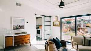 A modern living room with a sliding glass door leading to a patio, a white console table with books and a glass cover, and a brown sofa with cushions. - Glam Designer House with a Pool, Walk to Old Town (Scottsdale)