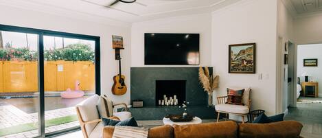 A modern living room with a fireplace, a ceiling fan, and a large window overlooking a garden.