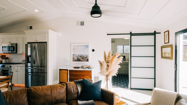 A modern kitchen with stainless steel appliances, a dining area with a brown leather couch, and a sliding glass door leading to a balcony. - Glam Designer House with a Pool, Walk to Old Town (Scottsdale)
