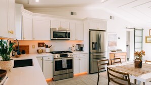 A modern kitchen with white cabinetry, stainless steel appliances, and a dining area with a wooden table and chairs. - Glam Designer House with a Pool, Walk to Old Town (Scottsdale)