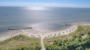Vista aérea de una playa con cielo despejado, mar tranquilo y una carretera que conduce a la orilla.