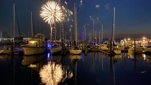 Un puerto deportivo de noche con barcos amarrados y fuegos artificiales en el cielo.
