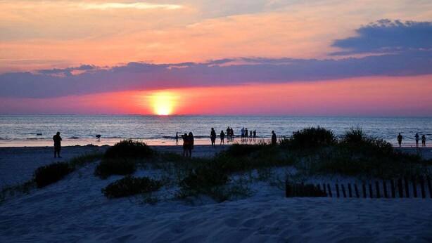 Escena de playa con gente caminando por la orilla durante el atardecer.