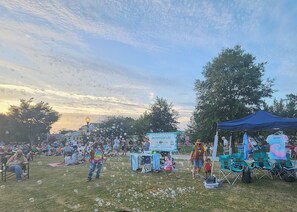 An outdoor event with a crowd, a sign, and a blue tent.