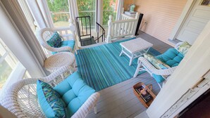 Un porche cubierto con muebles de mimbre, una mesita y vistas al verde exterior.