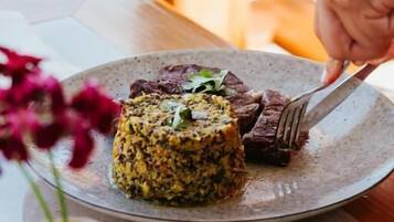 Un plato de comida con una mano sosteniendo un tenedor, sobre una mesa con un florero.