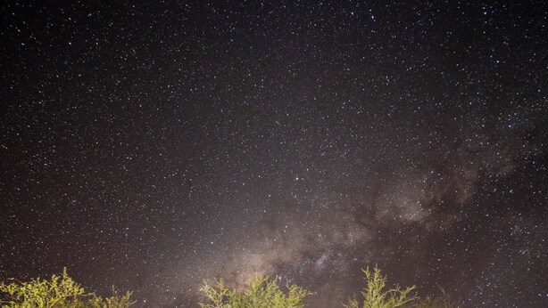 A wooden cabin with a covered porch, large windows, and a view of the night sky. - Hotel Tantakuy Eco Experience (Pozo Almonte)