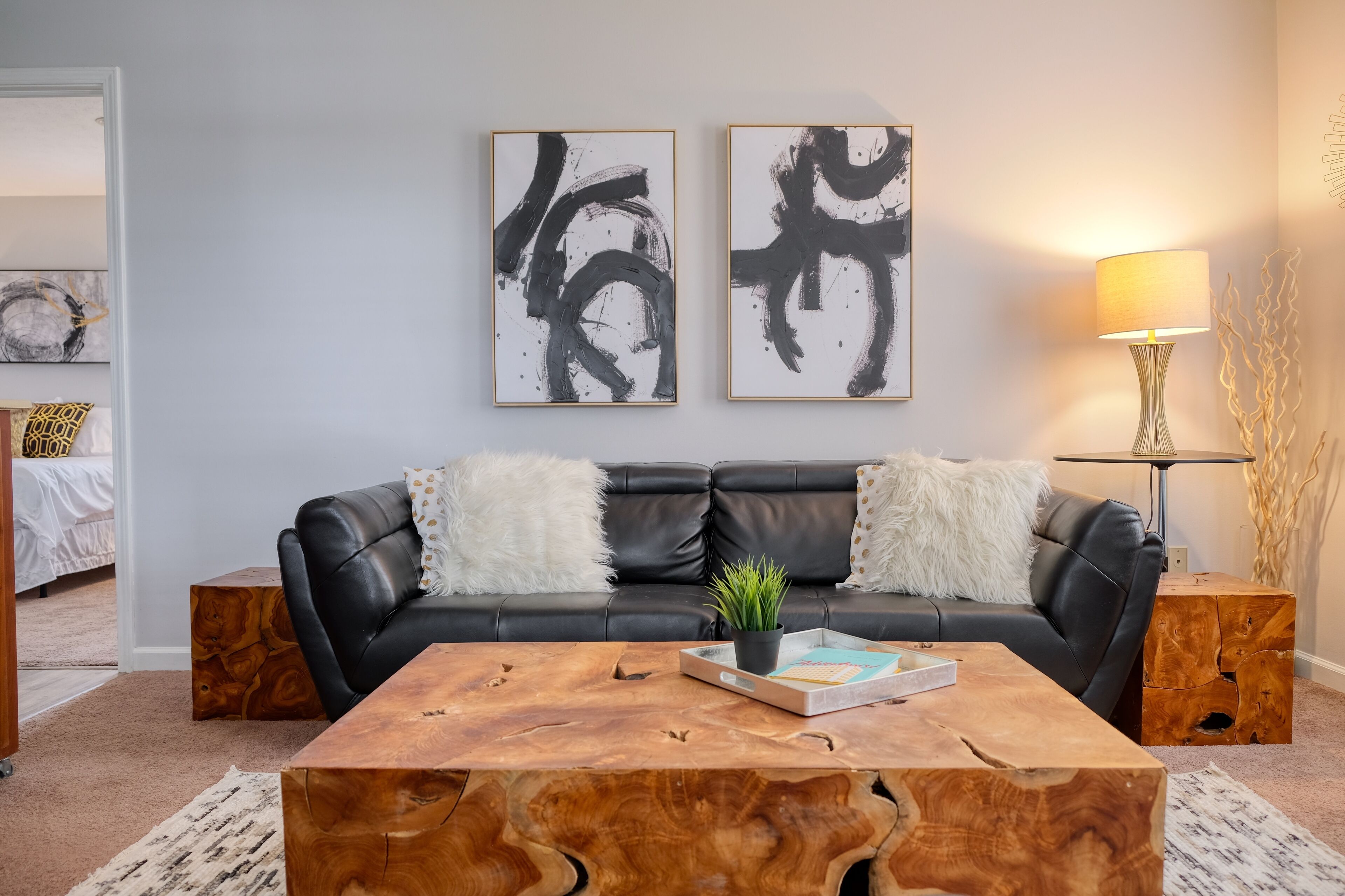 Ein modernes Wohnzimmer mit einer schwarzen Ledersofa, zwei abstrakten Gemälden, einem Holztisch und einer Stehlampe.