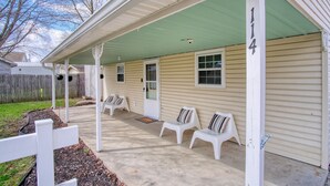 A covered porch with four white plastic chairs, a green roof, and a beige house number '114'.