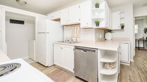 A modern kitchen with white cabinetry, a stainless steel dishwasher, and built-in shelves for plants.