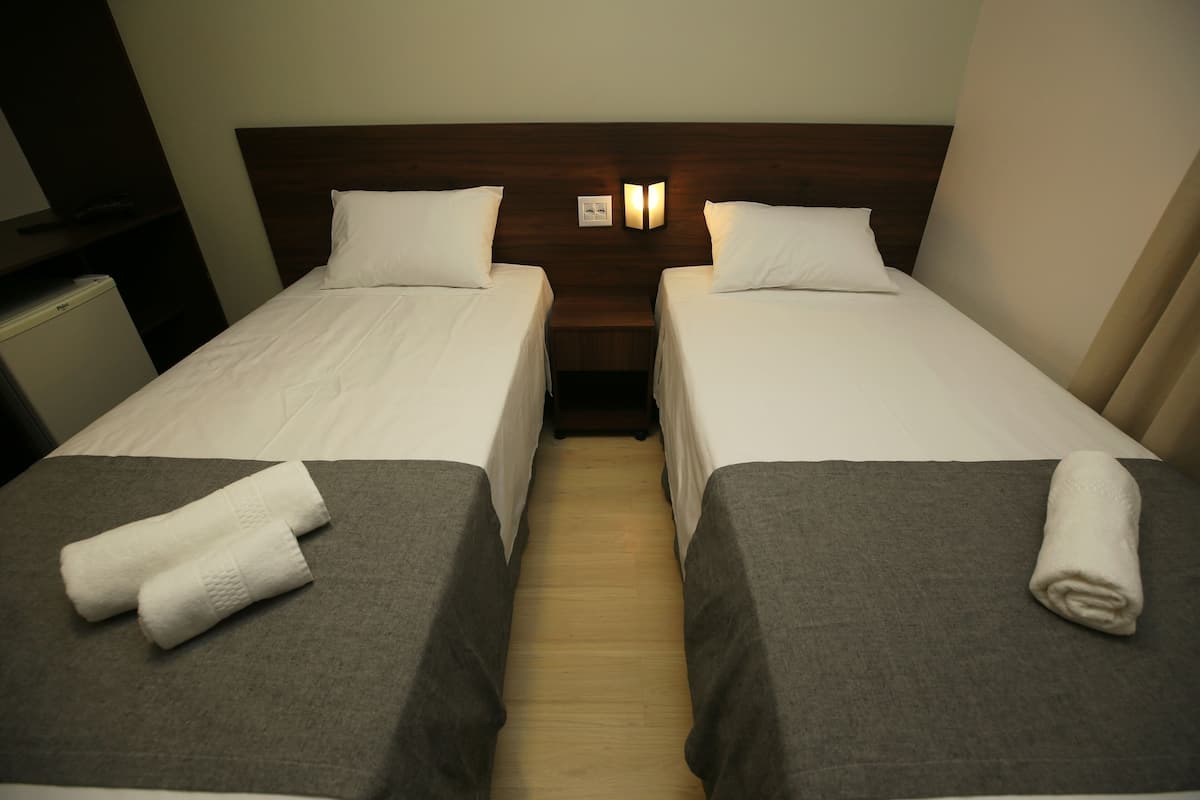 A hotel room with two single beds, a wooden headboard, a small bedside table, and a wall-mounted light fixture.