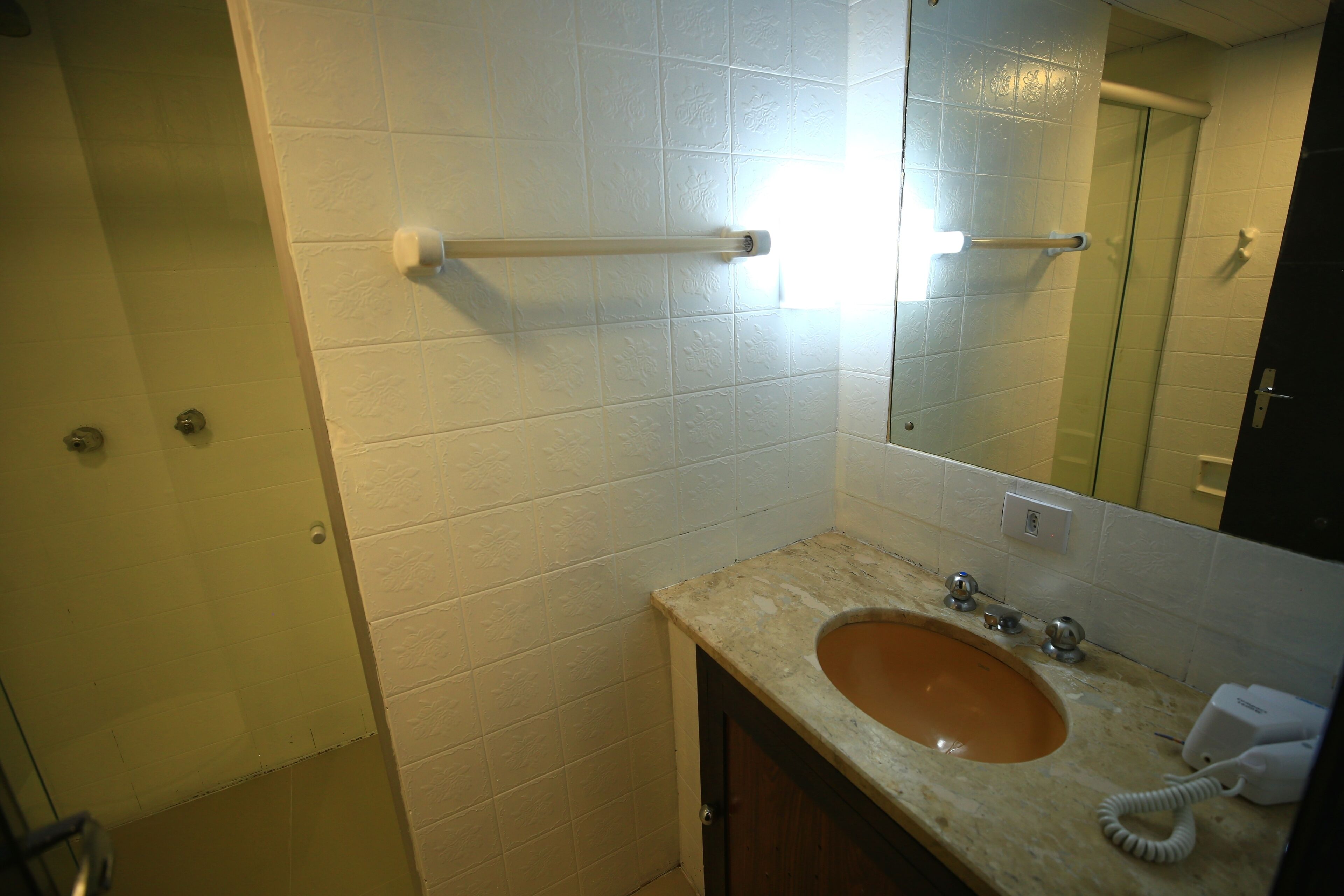 Une salle de bain avec un mur recouvert de carreaux blancs, un comptoir beige, un lavabo avec un miroir au-dessus et un distributeur de serviettes.