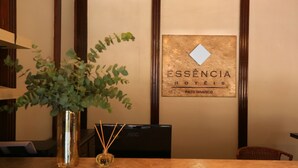Taulell de recepció amb una planta en test, un vas petit amb canyissos i un quadre amb el lema 'ESSENCIA HOTÉIS PATO BRANCO'.