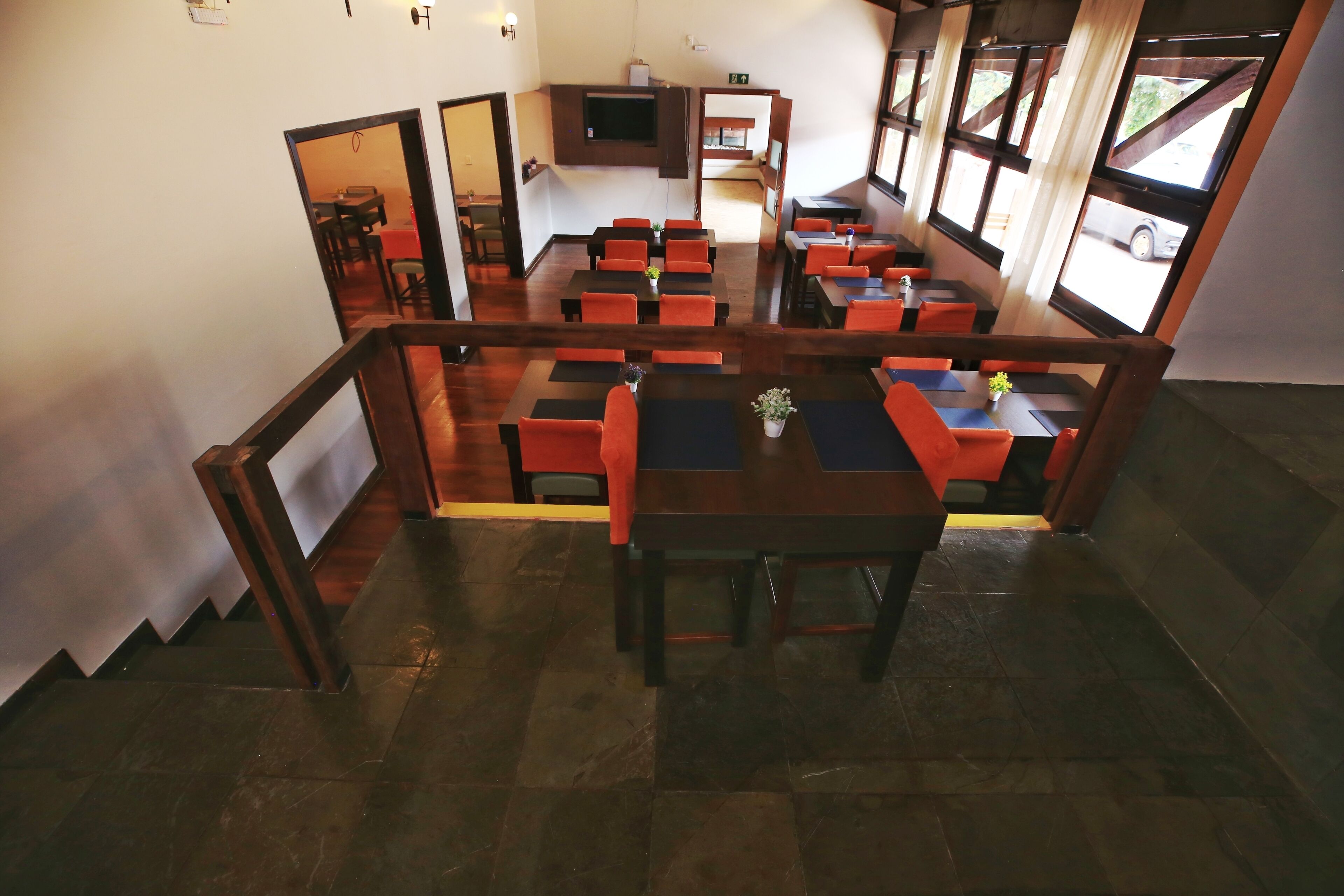 A restaurant with a central dining area, a TV mounted on the wall, and a staircase leading to an upper level.