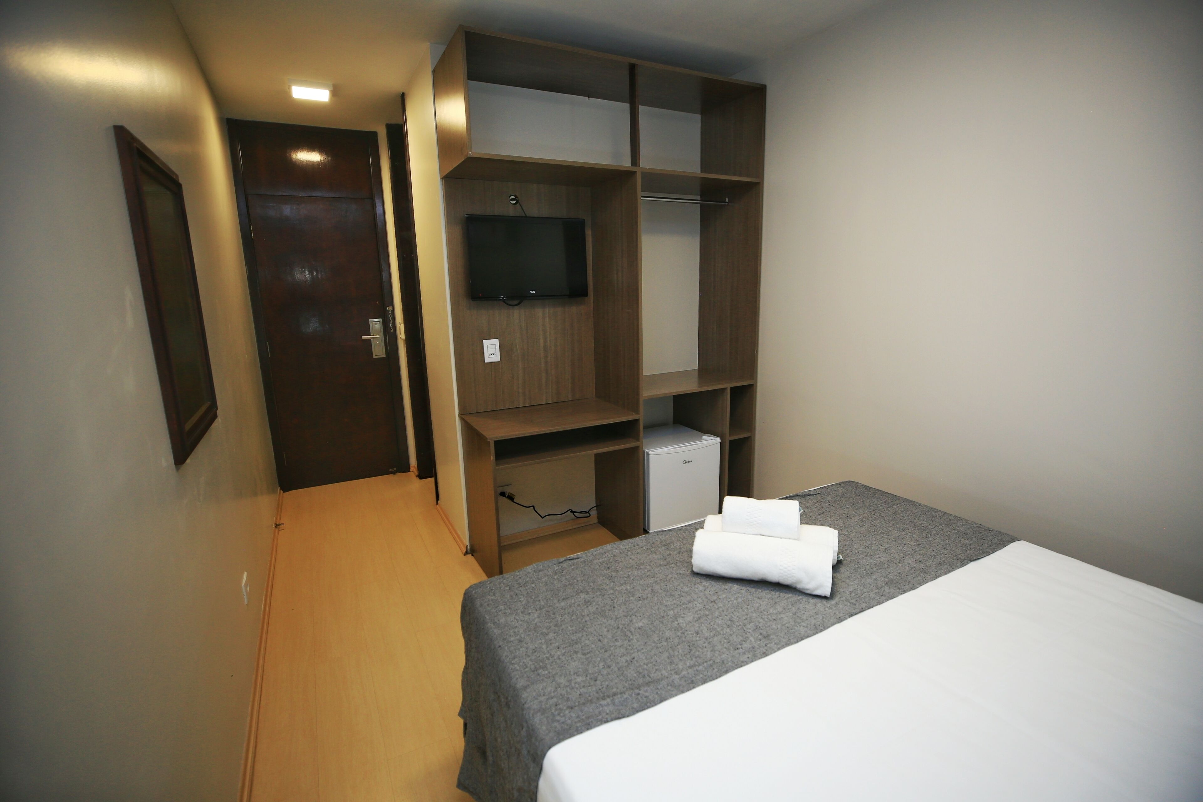 A hotel room with a bed, a TV mounted on the wall, and a wardrobe.