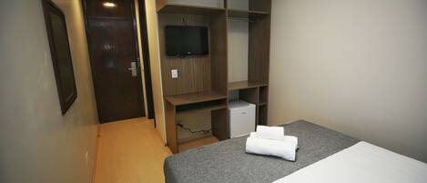 A hotel room with a bed, a TV mounted on the wall, and a wardrobe.