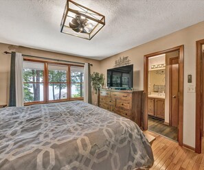 A bedroom with a large bed, wooden dresser, TV, and a bathroom visible through an open door.