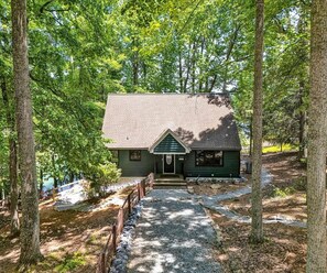 A cabin with a front porch, surrounded by trees, and a gravel path leading to the entrance.