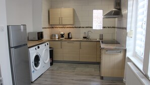 Een kleine keuken met een wasmachine, een magnetron, een koffiezetapparaat en een spoelbak.