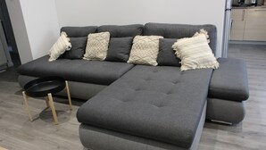 Een grijze hoekbank met vier kussens en een kleine zwarte fauteuil.