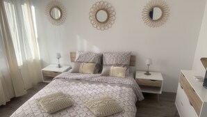 Een slaapkamer met een bed, twee nachtkastjes, een dressoir en drie spiegels aan de muur.