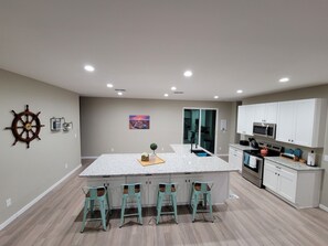 A modern kitchen with a large island, bar stools, white cabinets, and a ship's wheel decoration. - Paradise at Powell: Spacious home near Lake Powell (Page)