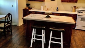 A kitchen with a central island, wooden cabinets, a clock, and a stove. - Secluded Cottage on Cattle Farm and Dog Friendly All Sizes (Vienna)