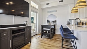 A modern kitchen with a large TV, dark cabinetry, a bar area with stools, and a view of the outdoors.