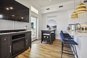 Una cocina moderna con un televisor grande, armarios oscuros, una zona de bar con taburetes y vistas al exterior.