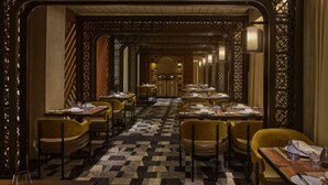 Ein Restaurant mit Schachbrettboden, Holzmöbeln und dekorativen Raumteilern. Die Tische sind mit Tellern und Gläsern gedeckt.