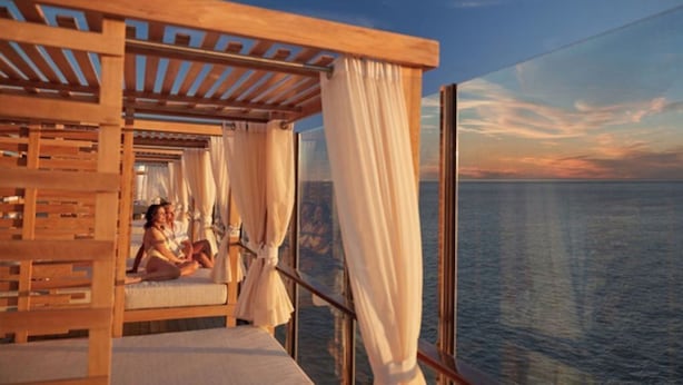 Ein Balkon mit einer Holzpergola und weißen Vorhängen, mit Blick auf ein Gewässer.