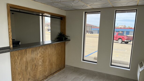 Zona de recepción con mostrador de madera, dos ventanas amplias y vista a un estacionamiento.