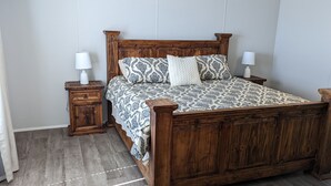 Un llit de fusta amb un sobrell i coixins estampats, flanquejat per les nits amb làmpades, en una habitació amb terra de fusta.