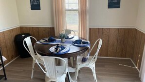Un coin repas avec une table ronde pour quatre personnes, des chaises blanches et deux éléments de décoration murale.