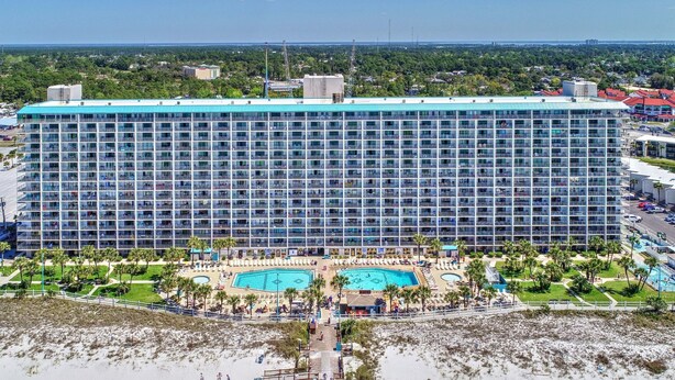A large hotel with multiple floors, a central pool area, and a beach with sun loungers. - Enjoy “BEACH LIFE”.  Breathtaking Beach Front Condo, Great Balcony & Amenities! (Panama City Beach)