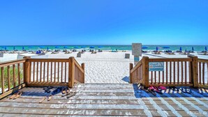 A wooden deck leading to a beach with umbrellas and lounge chairs. - Enjoy “BEACH LIFE”.  Breathtaking Beach Front Condo, Great Balcony & Amenities! (Panama City Beach)