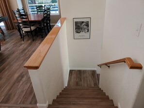 Un escalier en bois, doté d’une rampe, mène à un coin repas où se trouvent une table et des chaises en bois.