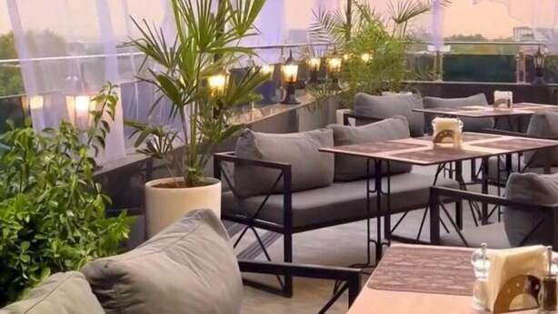 Un espace extérieur aménagé avec des bancs et des tables confortables, des guirlandes lumineuses et des plantes en pot.