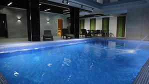 Une piscine intérieure à l’eau d’un bleu limpide, entourée de chaises noires et d’une table.
