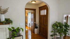 A hallway with wooden flooring, a white door with glass panels, a mirror with lights, and potted plants. - Gorgeous home outdoor covered bar  & minutes from floats, cliffs, tubing (Cabool)
