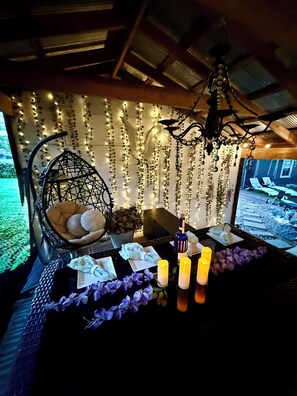 A cozy outdoor seating area with a hanging chair, candles, and a table set for dining. - Gorgeous home outdoor covered bar  & minutes from floats, cliffs, tubing (Cabool)