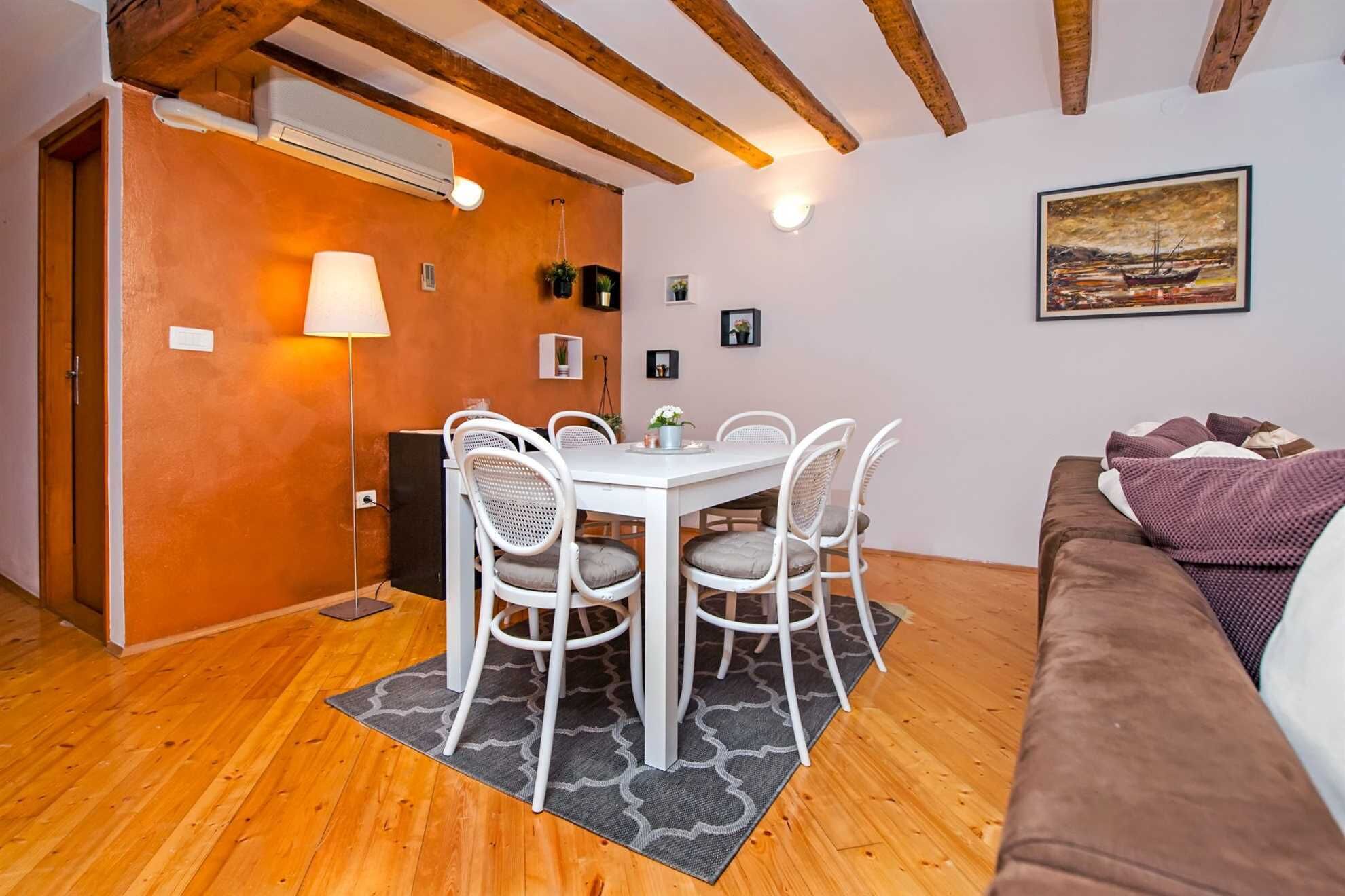 Um quarto acolhedor com teto de madeira, uma mesa de jantar com cadeiras brancas, um sofá marrom e um quadro na parede.