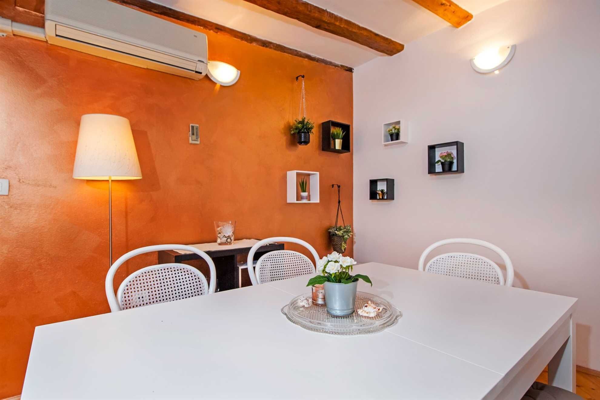 Un coin repas avec une table blanche, des chaises blanches, une lampe et des étagères murales ornées de plantes.