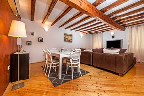 Ein gemütliches Wohnzimmer mit einer braunen Couch, einem Esstisch mit Stühlen, einem Fernseher und einer Lampe.