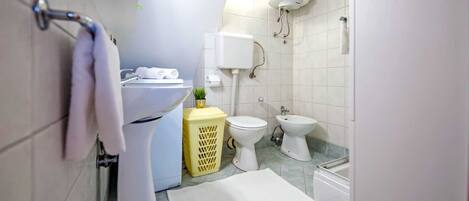 Een kleine badkamer met toilet, bidet en een wit wastafel.