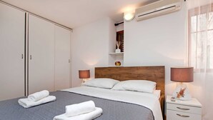 Una cama bien hecha con dos almohadas, una mesita de noche con lámpara, un armario y un equipo de aire acondicionado.